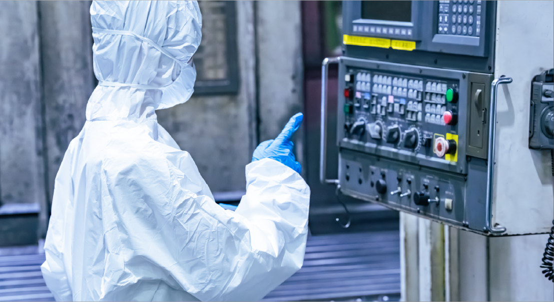 Worker in a white protective suit and blue gloves operating a metal control panel on an industrial machine.