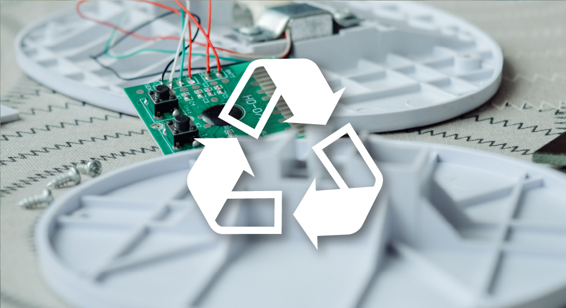White recycling symbol over a circuit board and disassembled electronic components, illustrating e-waste recycling concept.
